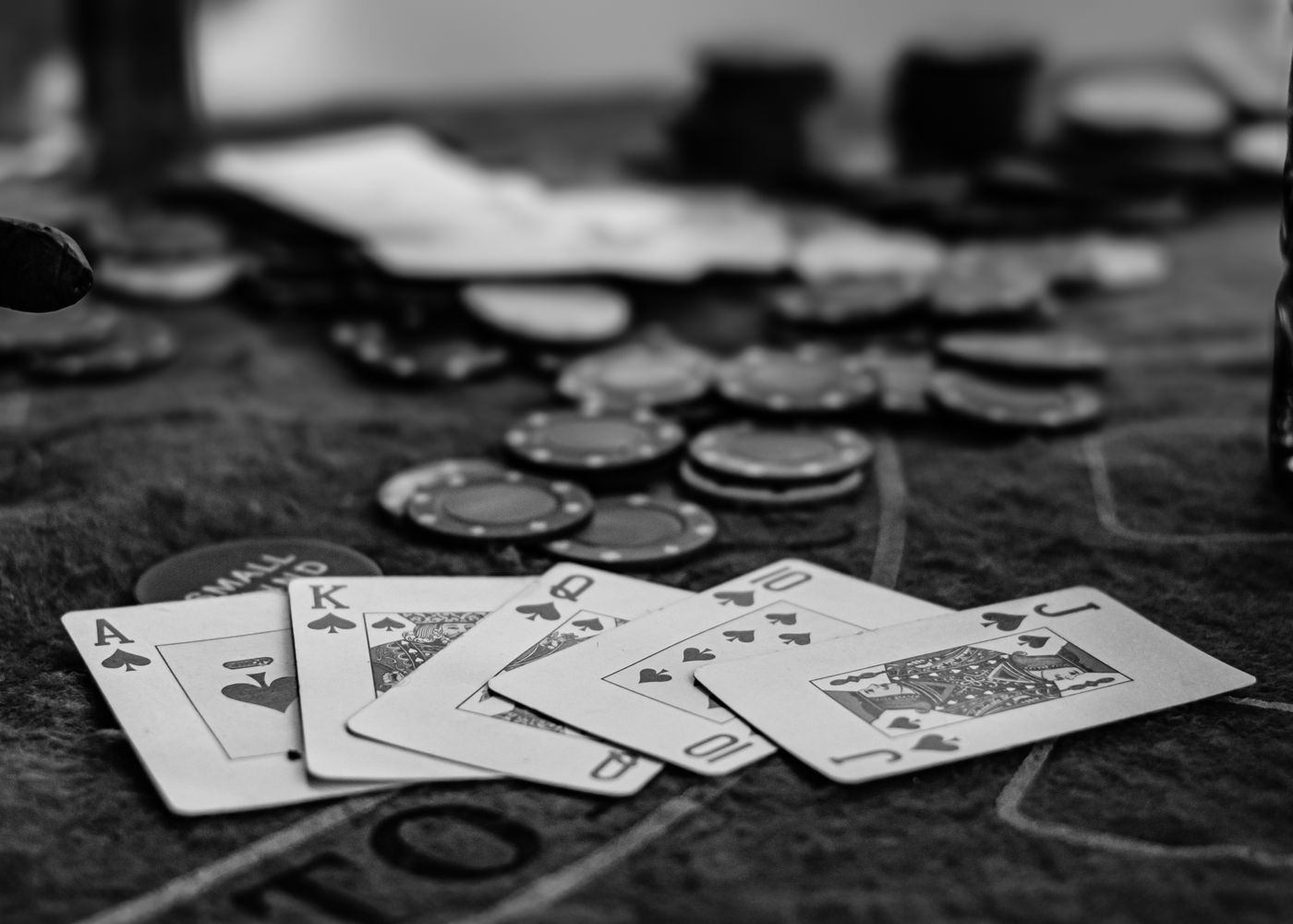Kartu remi dan chip poker di atas meja kasino dalam nuansa hitam putih