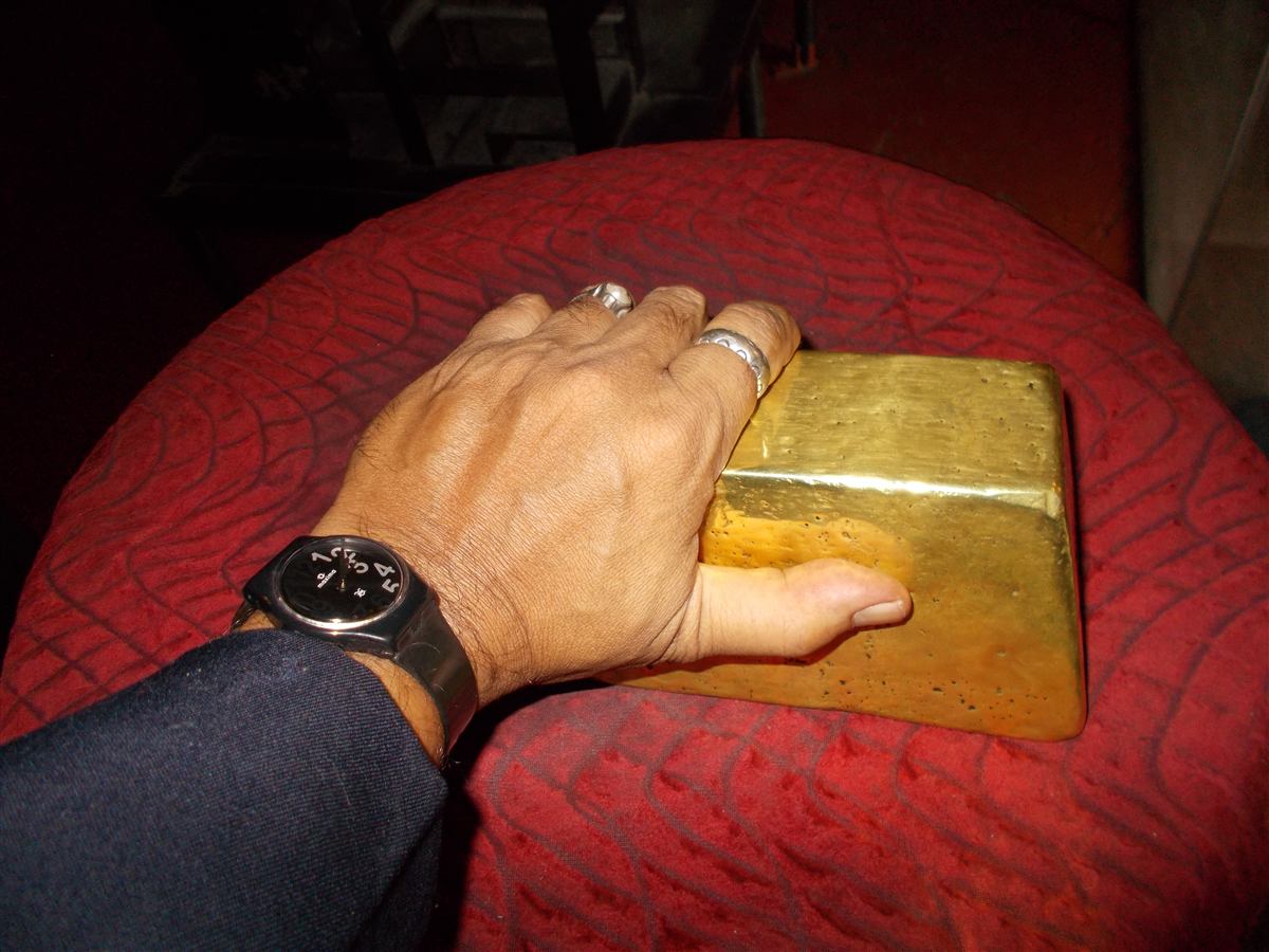 Tangan manusia menyentuh batangan emas besar