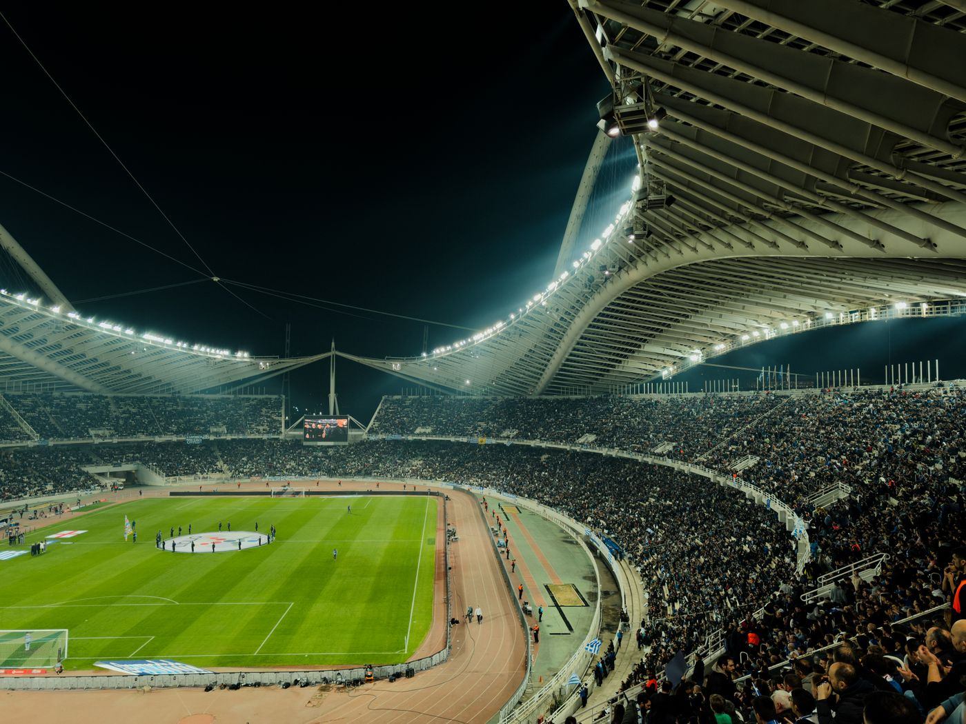 Stadion sepak bola menyala di malam hari dengan penonton memenuhi tribun